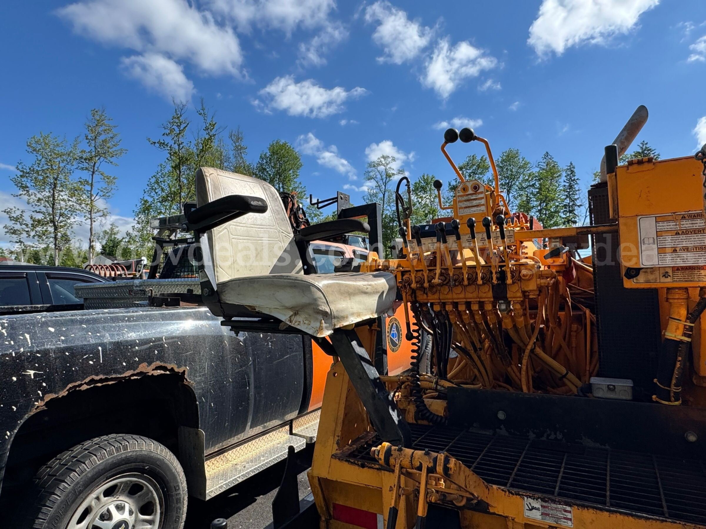 Truck-mounted asphalt hot oil heater with operator seat and control levers in view; yellow equipment attached to a black pickup truck.