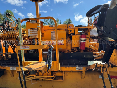 Mack asphalt paving truck in-service showing operator platform and safety rails, with hoses, control panels, and a fire extinguisher mounted on the side.
