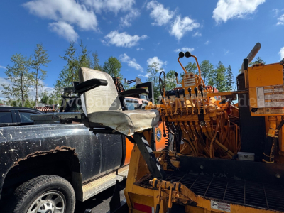 Truck-mounted asphalt hot oil heater with operator seat and control levers in view; yellow equipment attached to a black pickup truck.