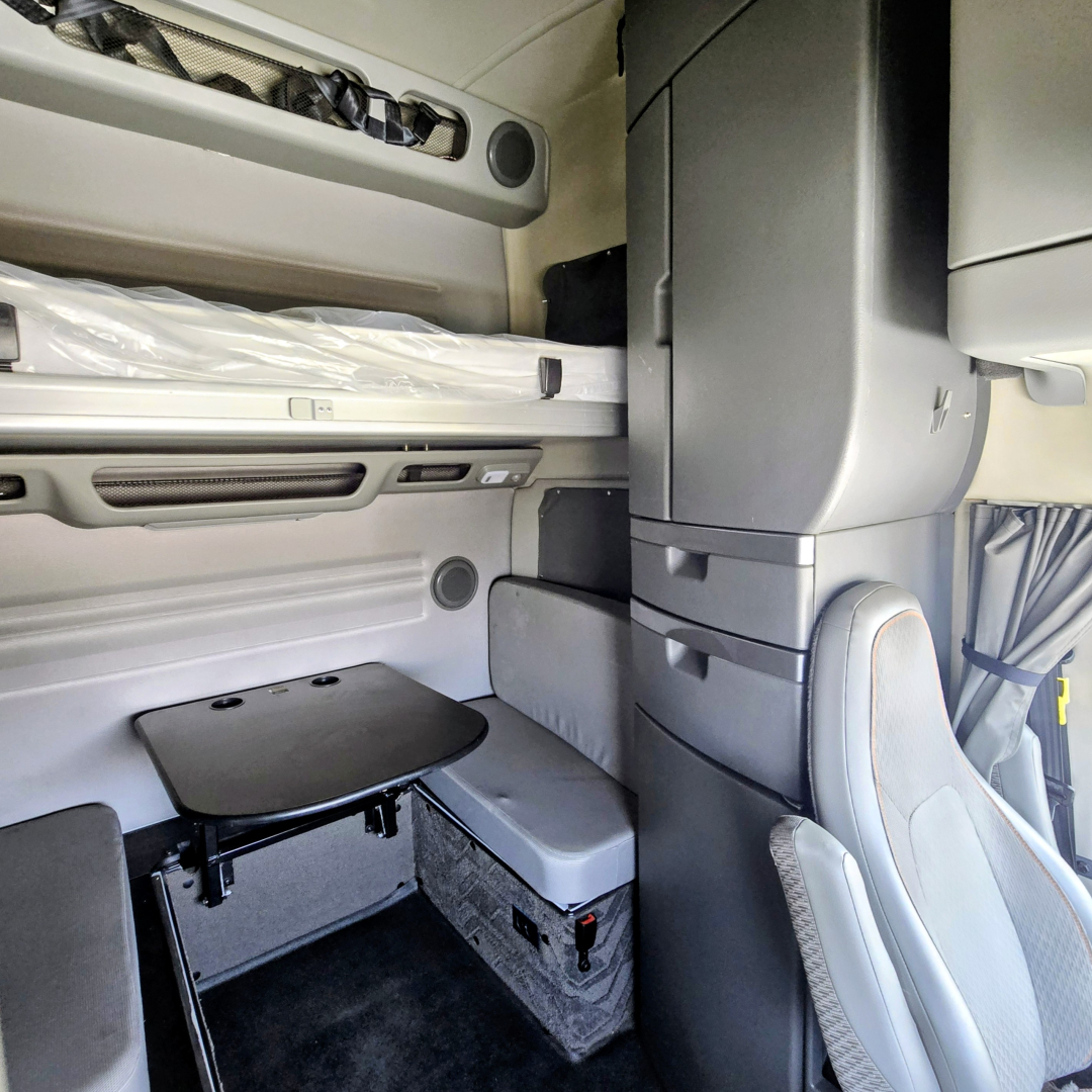 Volvo VNL sleeper cab interior showing bunk bed and storage cabinet with table and seating area.