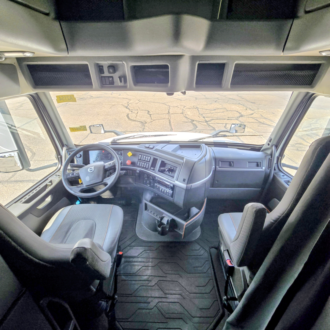 Cab interior of a Volvo VNL64T860 truck showing the steering wheel, dashboard, and two seats from a front-facing camera view.