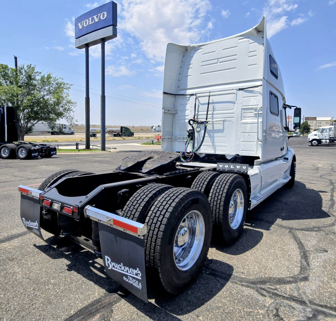 Rear-angled view of 2022 Volvo VNL64T860 sleeper tractor showing cab, chassis, and dual rear axles; visible text includes Volvo sign in background and Bruckners mudflaps.