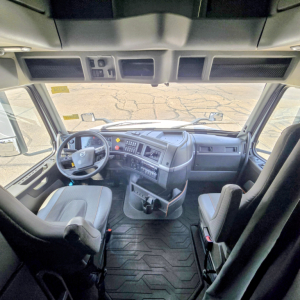 Cab interior of a Volvo VNL64T860 truck showing the steering wheel, dashboard, and two seats from a front-facing camera view.