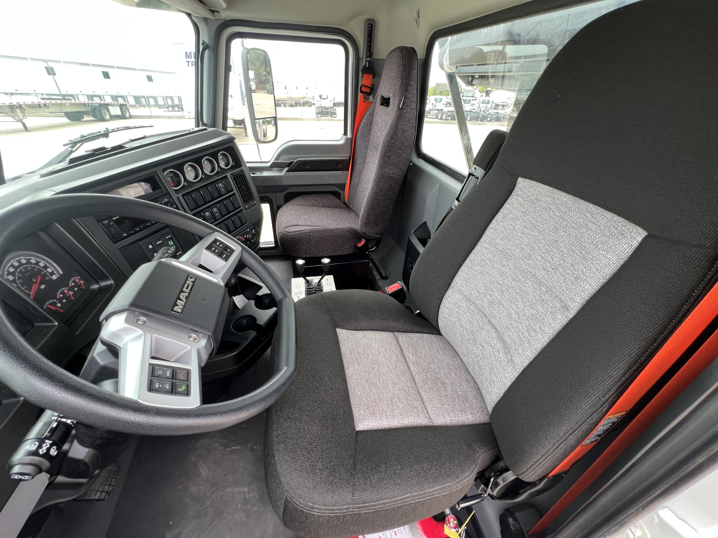 Interior of a 2027 Mack GR64B truck cab showing steering wheel, dashboard gauges, and driver seat with grey fabric.