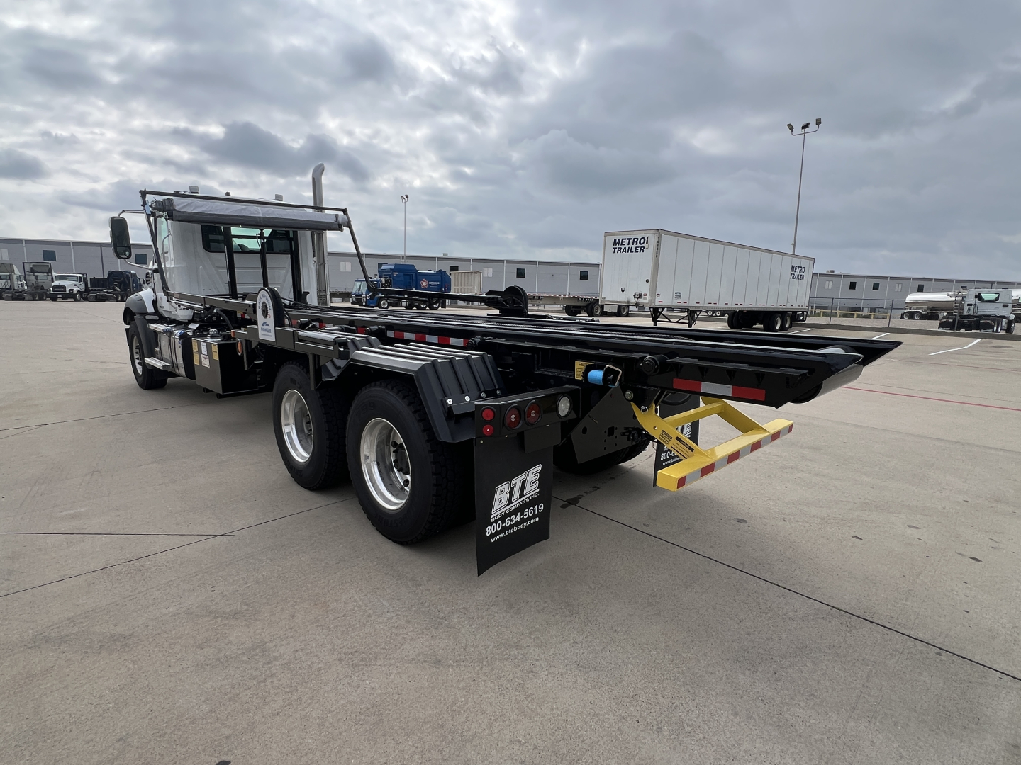 Mack GR64B roll-off truck chassis and rear section with yellow rear bumper protection and black mud flaps.