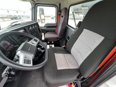 Interior of a 2027 Mack GR64B truck cab showing steering wheel, dashboard gauges, and driver seat with grey fabric.