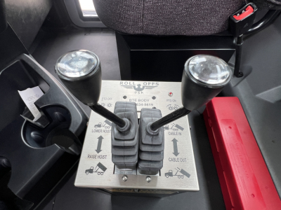 Mack GR64B rollover truck cab interior showing roll-off control lever panel with two joysticks and labeled switches.