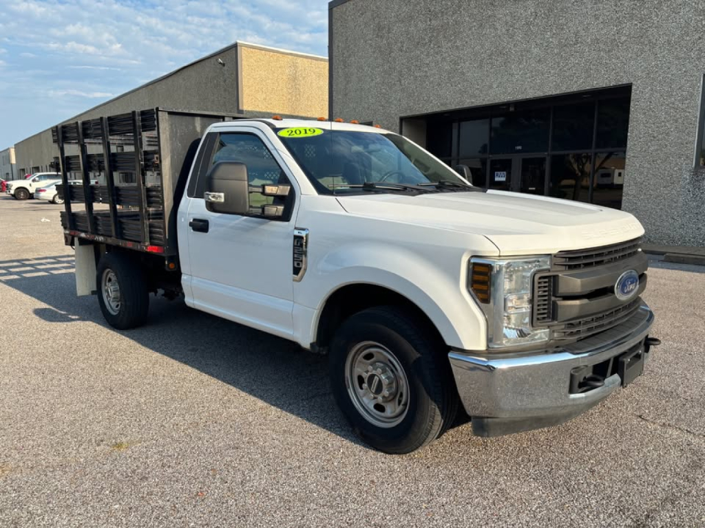Ford F-250 regular cab stake bed truck in white, front three-quarter view, 2019 model, with utility flatbed and black cage.