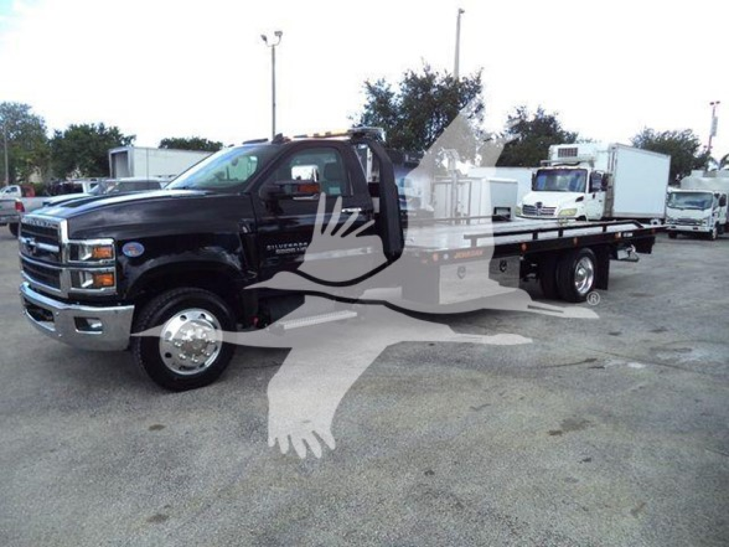 Truck image of a black 2023 Chevrolet Silverado 6500HD rollback tow truck with extended flatbed, front grille, headlights, and side mirrors visible.