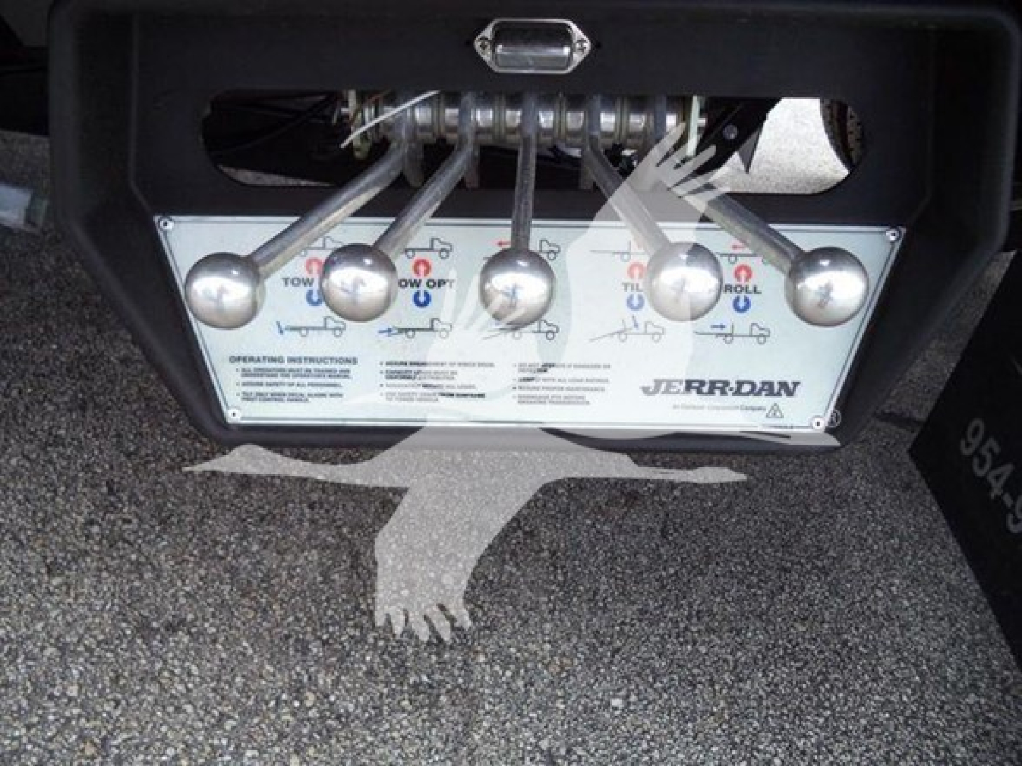 Trailer/hookup control panel with multiple levers and labels under a tow truck bed, showing Jerr-Dan branding and operation instructions.
