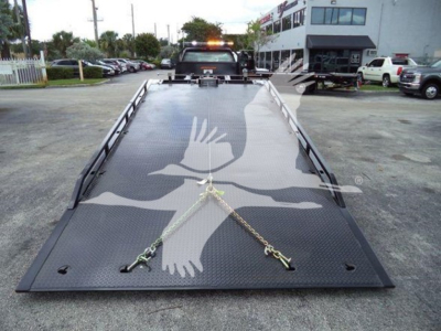 Tow truck flatbed with a Chevrolet Silverado 6500HD banner on ramp surface showing safety chains and metal deck.