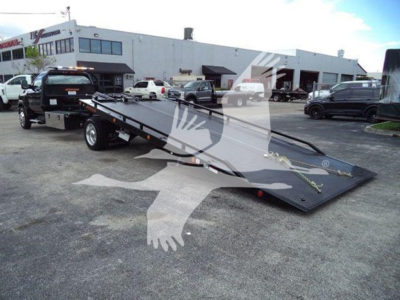 Tow truck rollback flatbed with Chev Silverado 6500Hd branding, tilt-bed ramps visible in foreground, dealership lot in background.