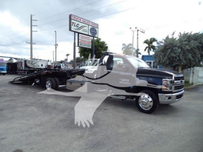 Black and silver 2023 Chevrolet Silverado 6500HD rollback tow truck with extended cab and flatbed, front grille, chrome bumper, in dealership lot.