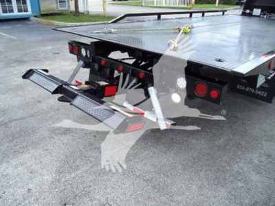 Flatbed tow truck rear with dual drop-down ramps and LED taillights; yellow strap securing front, steel platform, heavy-duty bumper, hydraulic components visible.