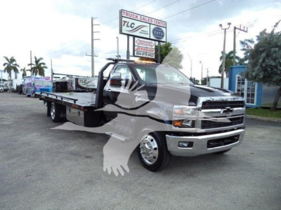 Truck image showing a 2023 Chevrolet Silverado 6500HD rollback tow truck with a large flatbed, chrome bumper, and stacked lettering on the Silverado grille.