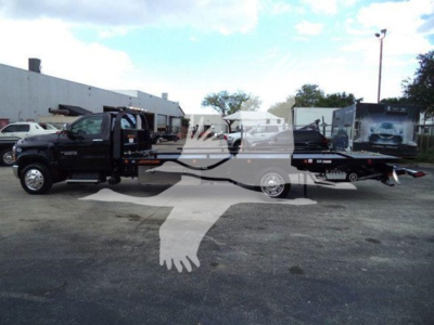 Truck bed tow truck setup showing Chevrolet Silverado 6500HD with rollback bed and towing equipment, dark color, side view