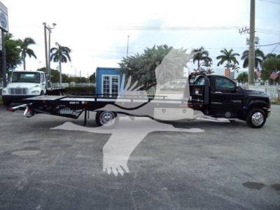Truck with car carrier/rollback bed attached, black cab on right, white cab on left, palm trees in background.