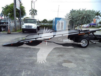 Flatbed rollback tow truck with low-profile trailer and a white cab in background.