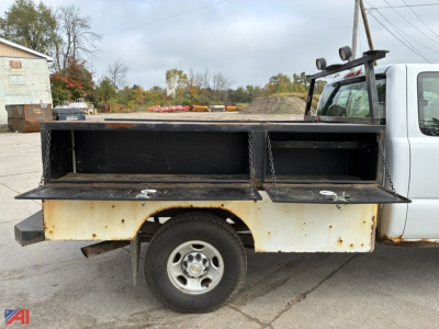 Truck bed of a 2006 Chevrolet Silverado 2500 utility/service body with open compartments and chain latches; white cab, rust on lower panel, 2wd, single rear wheel.