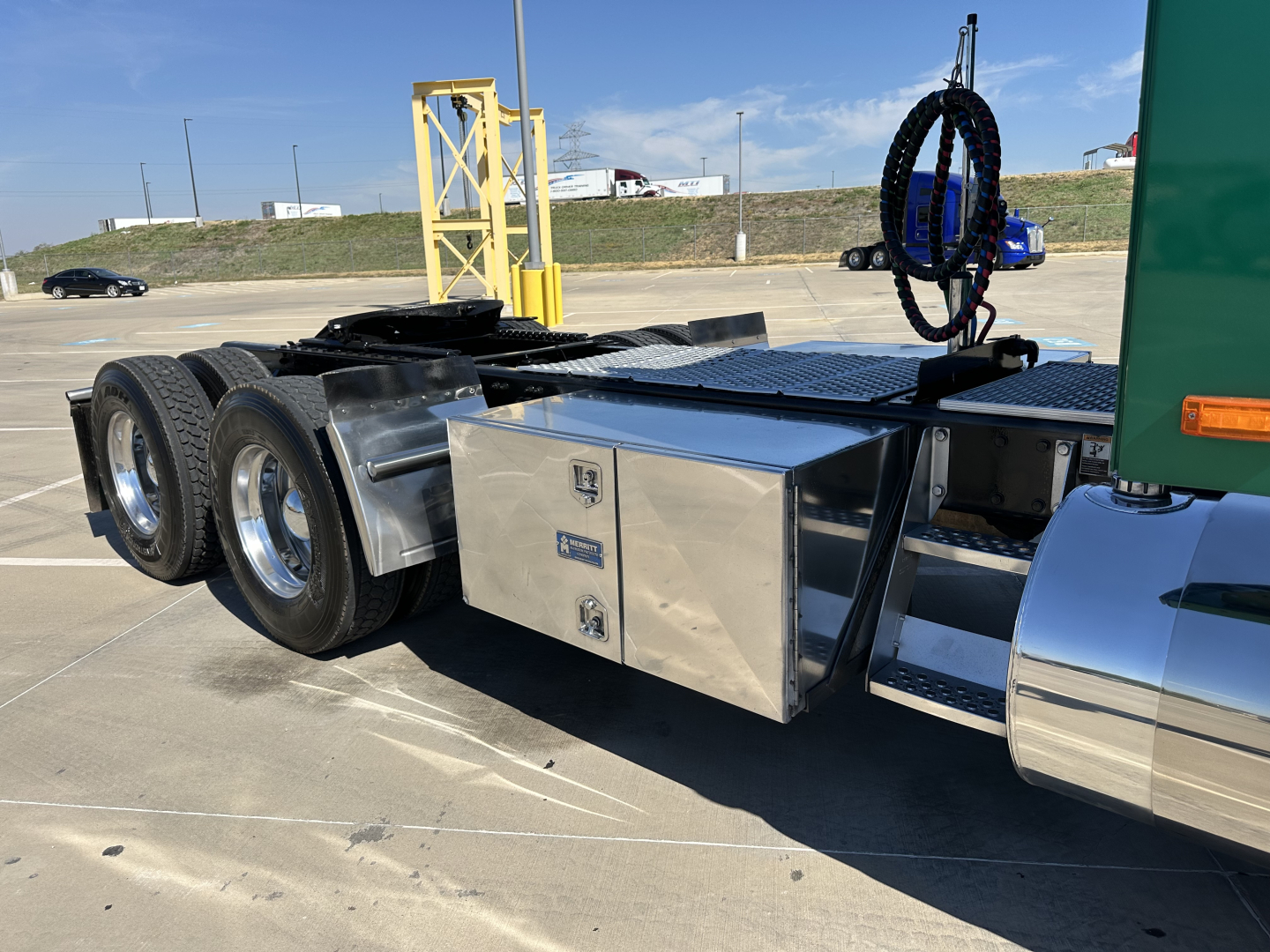 Kenworth T680 chassis side view showing aluminum toolbox, fuel tanks, dual rear axles, and air lines with yellow support structure in background.