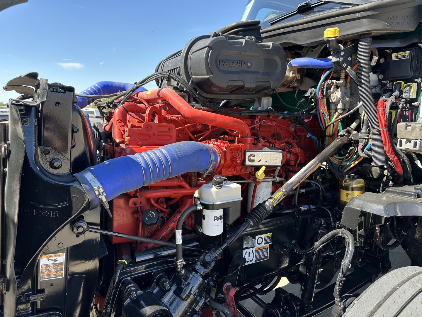Kenworth T680 engine bay with red engine, blue intercooler hose, and assorted wiring and components visible.