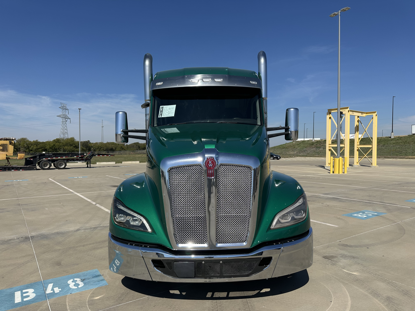 Kenworth T680 front view in green with chrome grille and bumper; large side mirrors and tall exhaust stacks visible in a parking lot.