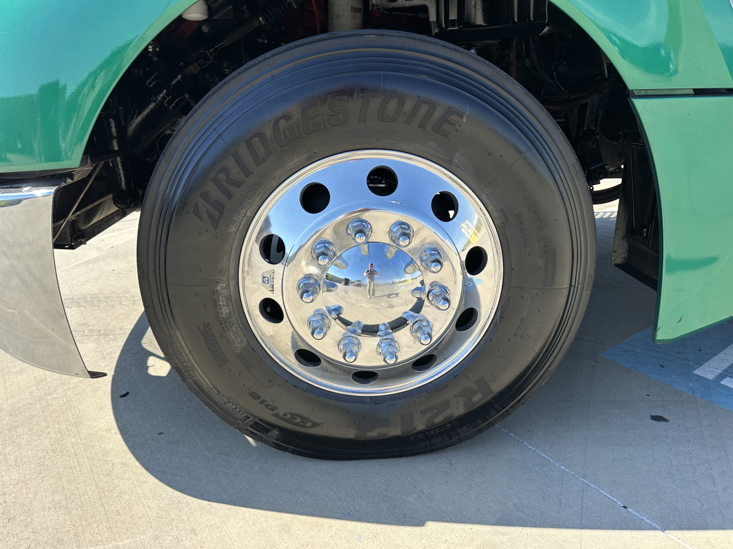 Kenworth T680 front wheel and tire showing Bridgestone tire with chrome hub and green fender