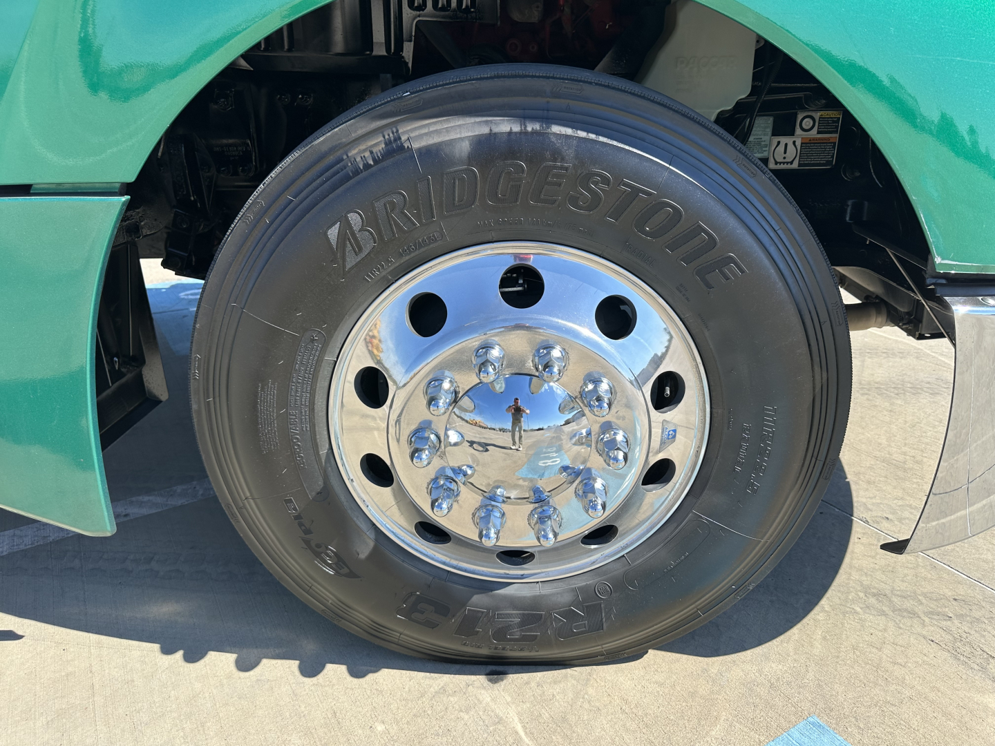 Front wheel of a green Kenworth T680 showing Bridgestone tire and chrome hub with lug nuts.