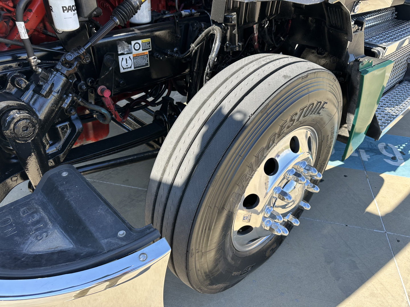 Kenworth T680 front wheel and suspension showing dual tires and steering linkage with tire branding visible.