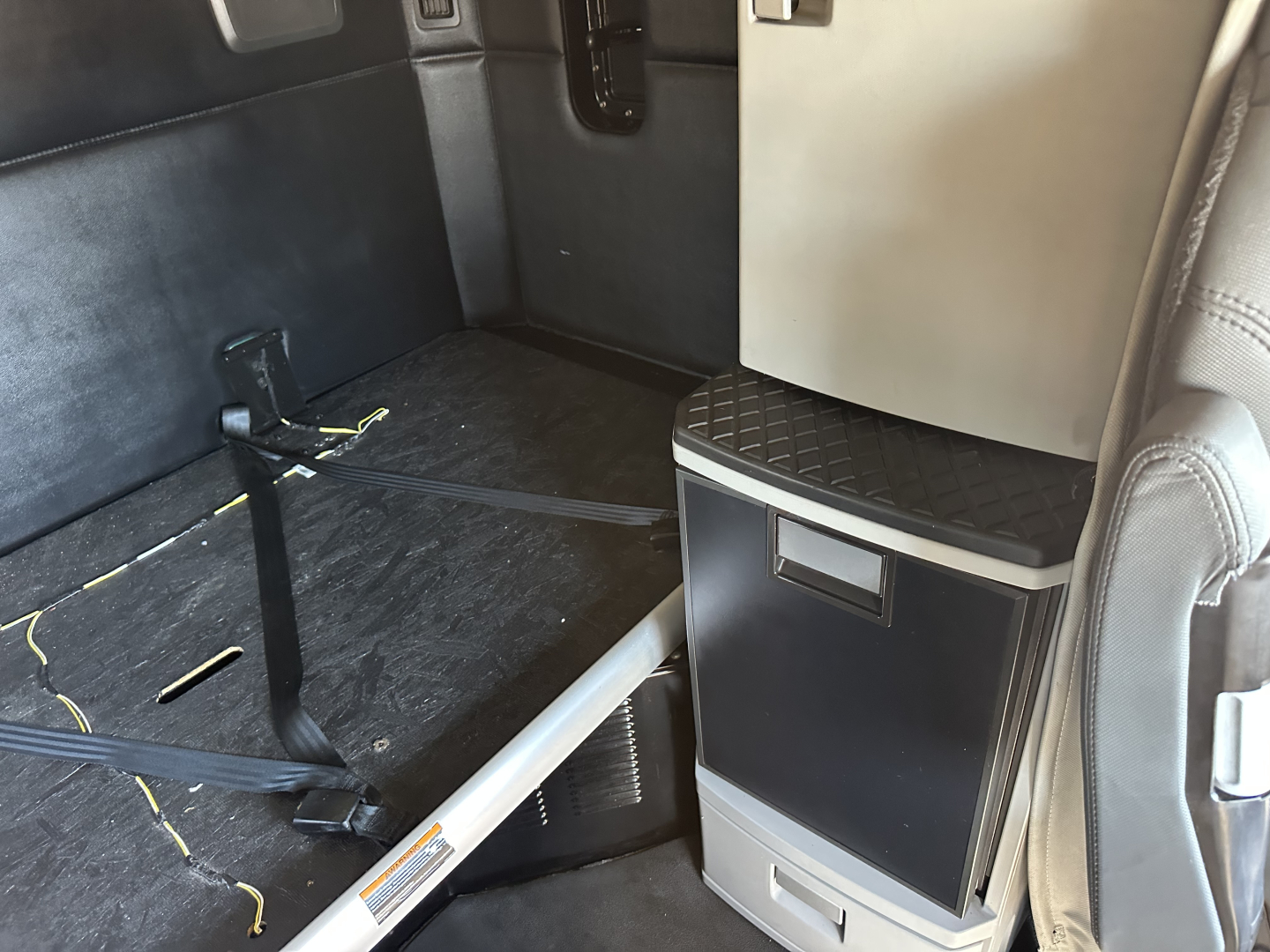 Kenworth T680 interior cargo area with storage cabinet and sleeper space, showing black floor, seatbelt, and metallic cabinet near door.