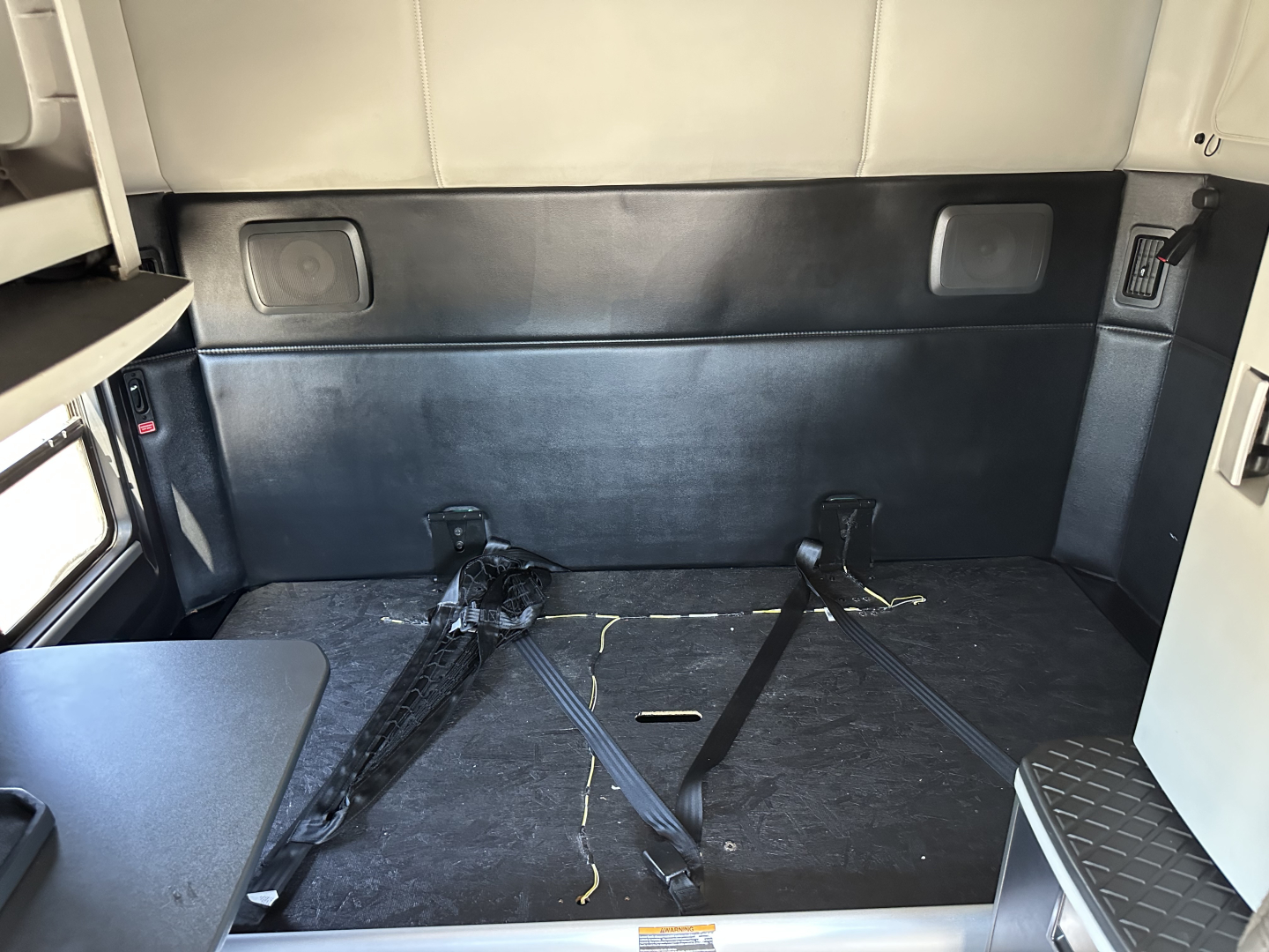 Kenworth T680 sleeper cab interior cargo area with tie-downs and black flooring.