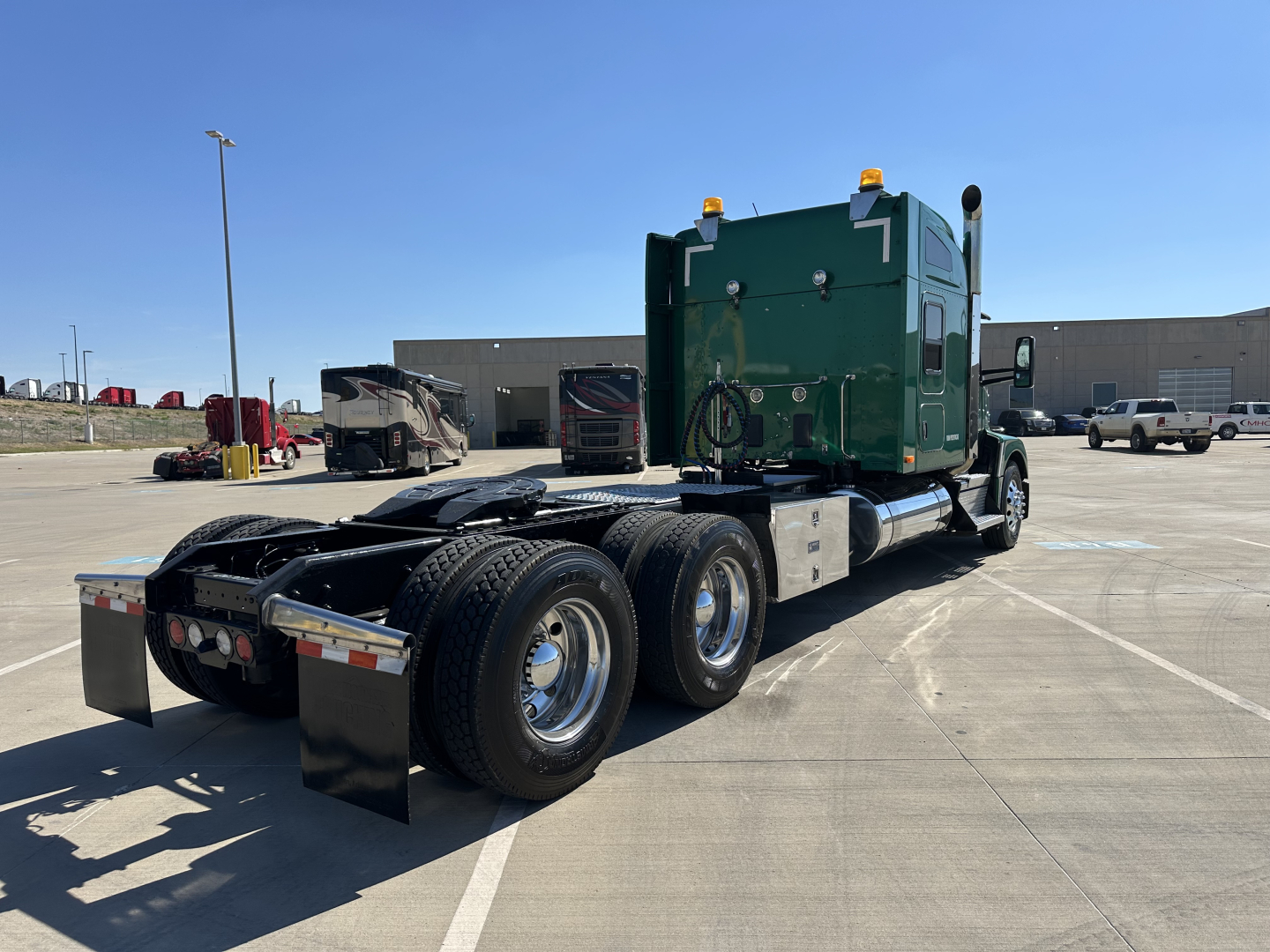 Kenworth T680 tractor in a parking lot, side view showing green cab, dual rear axles, and fifth wheel setup.