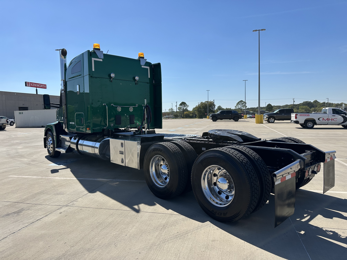 Kenworth T680 truck tractor from rear-left angle showing green sleeper cab, dual rear axles, chrome wheels, and flatbed with mirror reflections.