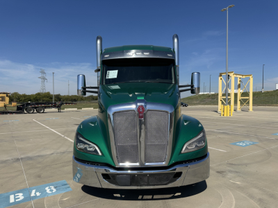 Kenworth T680 front view in green with chrome grille and bumper; large side mirrors and tall exhaust stacks visible in a parking lot.