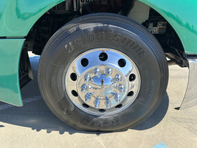 Front wheel of a green Kenworth T680 showing Bridgestone tire and chrome hub with lug nuts.