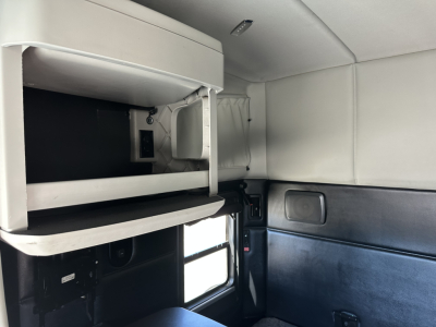 Kenworth T680 sleeper cab interior featuring upper storage shelf and window, with light gray ceiling and black lower wall panels.