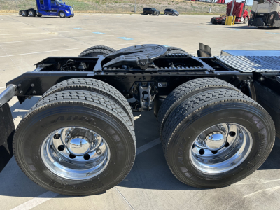 Kenworth T680 chassis rear view showing dual rear axles with chrome wheels and heavy-duty tires, visible battery box area and hitch mounting in the frame.