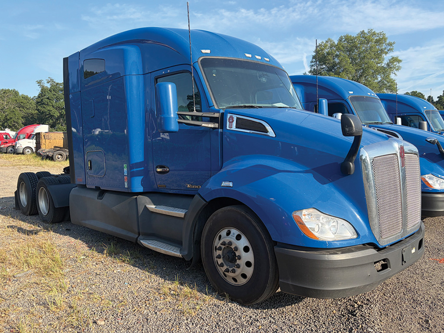Blue 2019 Kenworth T-680 conventional daycab truck side view showing twin rear axles, aerodynamic sleeper, and large chrome grille.