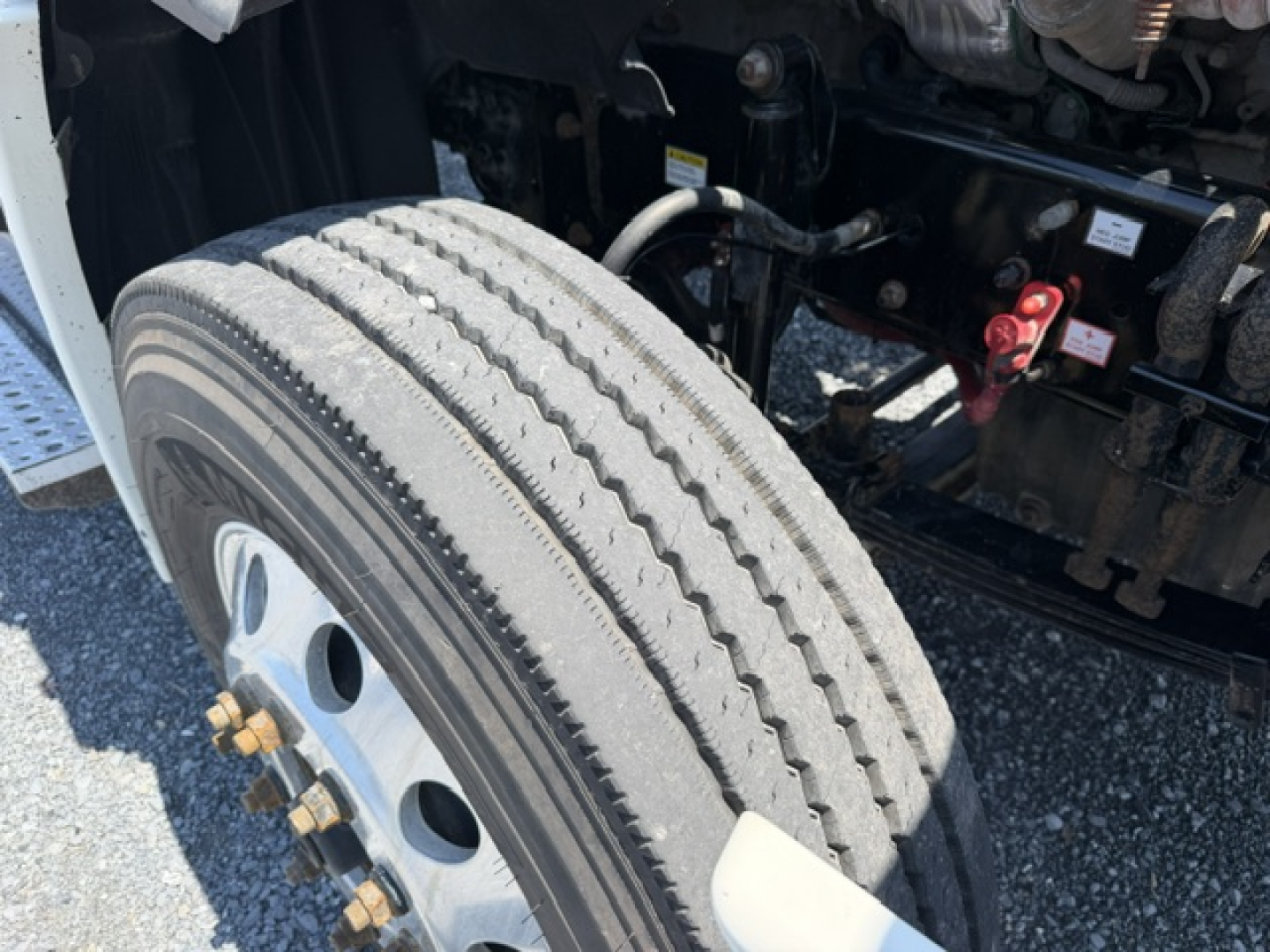 Truck wheel and front suspension area of a Freightliner Cascadia CA125DC, showing front tire tread and wheel studs, part of the engine bay and frame in view.