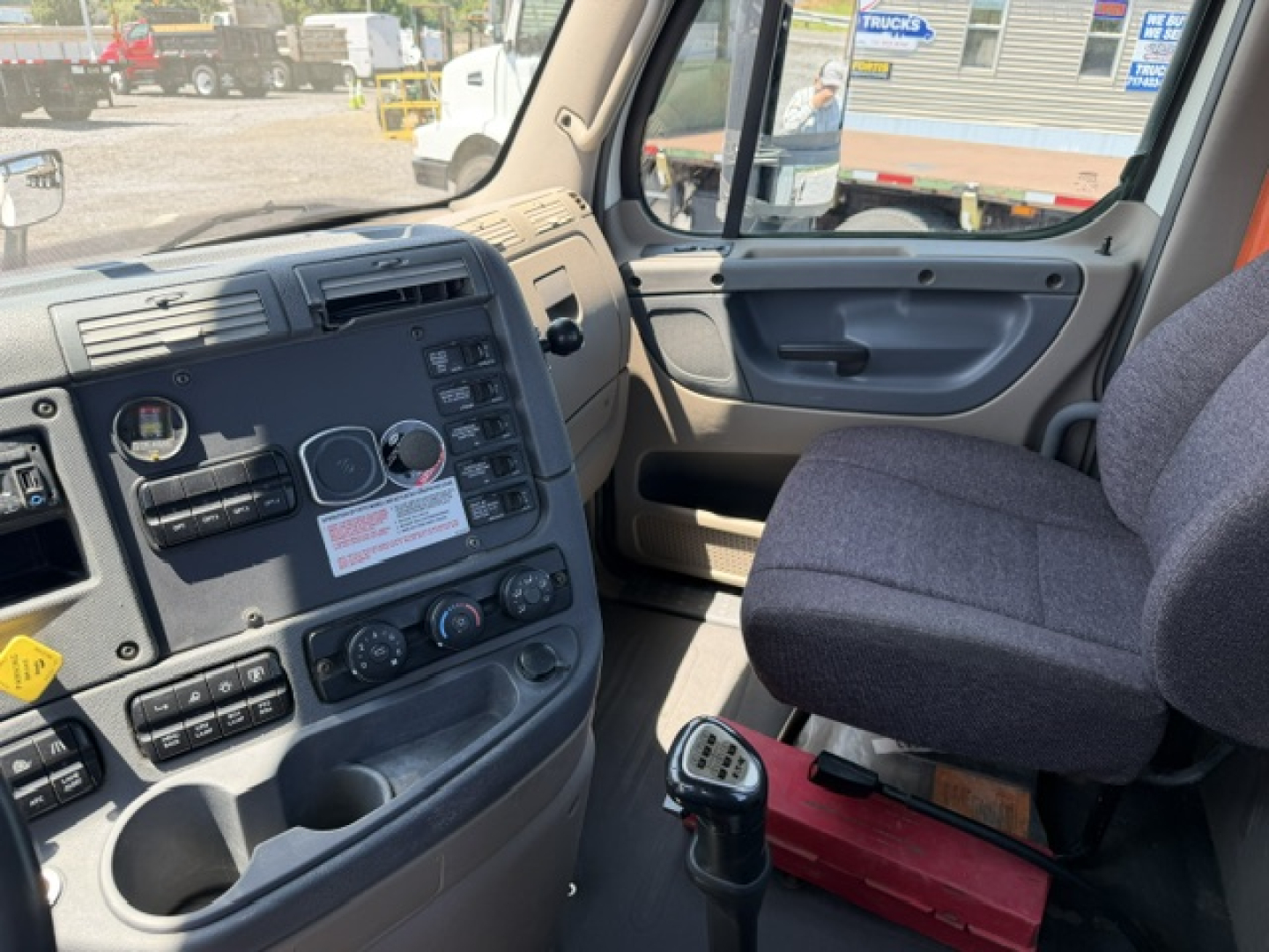 Interior of Freightliner Cascadia truck cab showing dashboard gauges, control panel, and driver seat with gear shifter in foreground.
