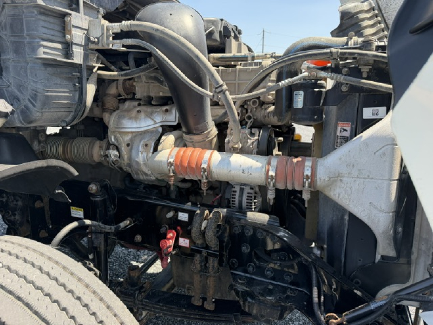Diesel truck engine bay showing Freightliner Cascadia components with hoses, alternator, and exhaust pipe in view; tag details not legible.