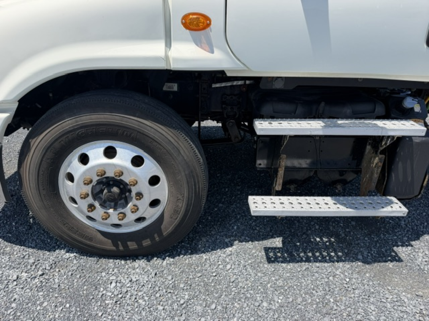 Front left wheel and entry steps of a Freightliner Cascadia truck showing aluminum wheel, front fender, and side steps with riveted tread pattern.