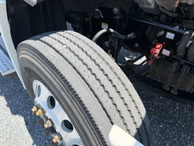 Truck wheel and front suspension area of a Freightliner Cascadia CA125DC, showing front tire tread and wheel studs, part of the engine bay and frame in view.