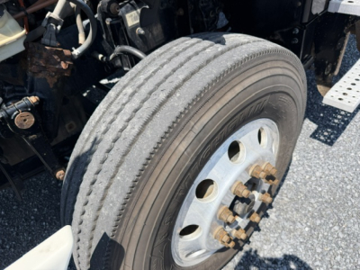 Truck wheel and front axle of a Freightliner Cascadia with dual rear tires and wheel bolts, showing tire tread and hub area.