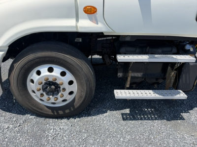 Front left wheel and entry steps of a Freightliner Cascadia truck showing aluminum wheel, front fender, and side steps with riveted tread pattern.