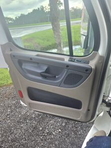 Truck cab interior door panel of a 2017 Freightliner Cascadia single axle showing beige/gray plastic interior with window controls and speaker grill.