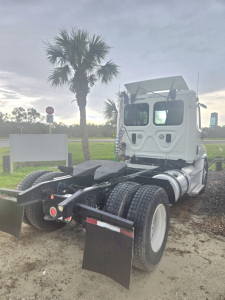 Truck rear view showing fifth wheel undercarriage and dual rear axles on a white Freightliner Cascadia daycab with mud flaps.