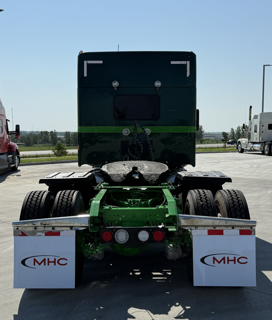 Kenworth W990 truck cab rear view showing green chassis and dual rear axles with mud flaps bearing MHC logos.