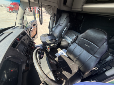 Kenworth W990 truck interior showing driver's seat, steering wheel, dashboard, and passenger seat with curtains; center console and controls visible.