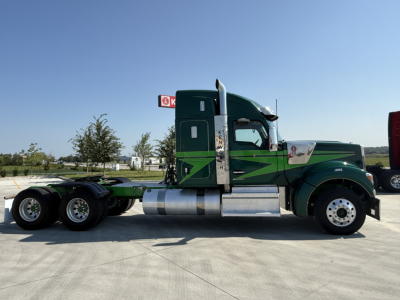 Side view of a 2023 Kenworth W990 tractor truck in green with chrome fuel tanks and black chassis, showing no visible text labels on the cab side.